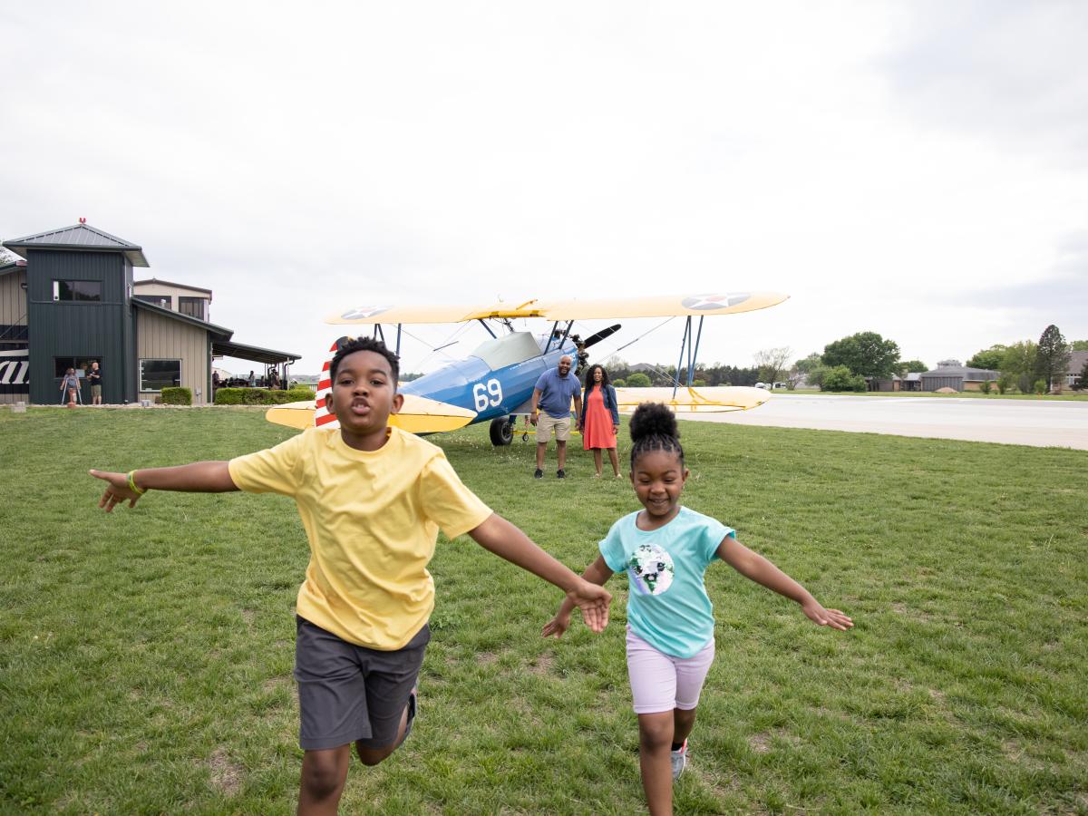 Kids run in a field by a plane at Stearman Airfield in Benton, Kansas