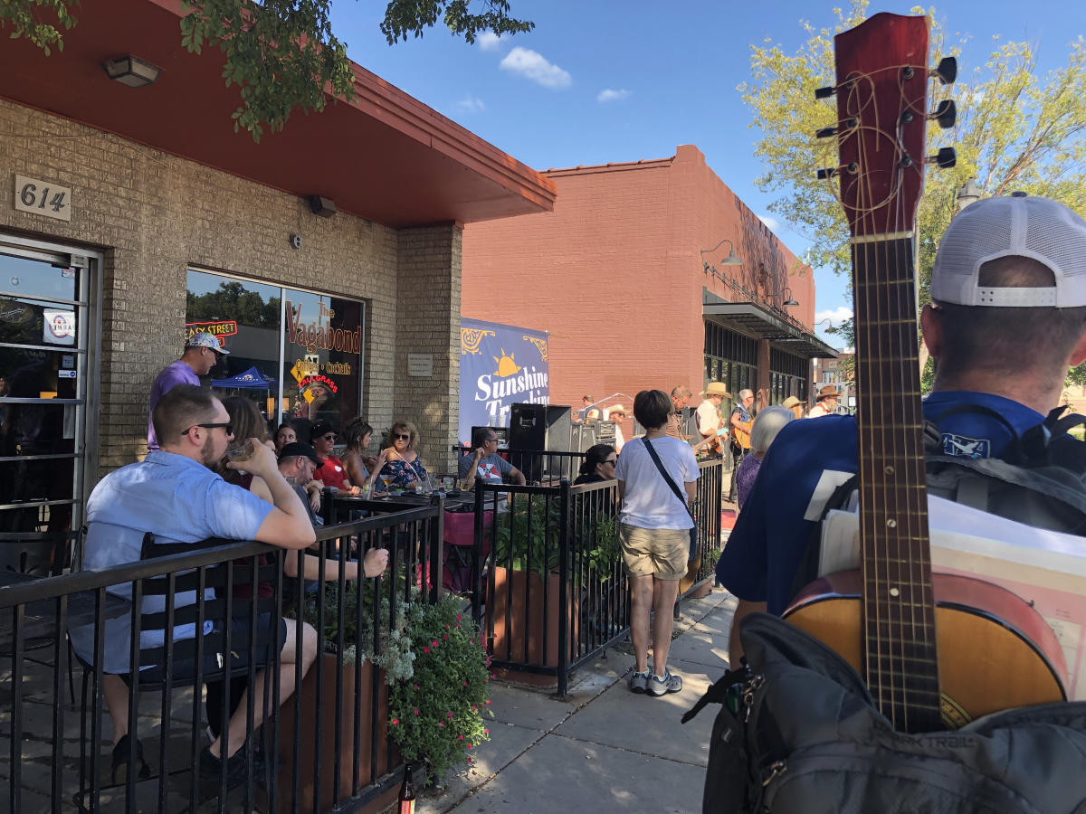 People enjoy drinks and food on an outdoor patio on a sunny day in Delano District