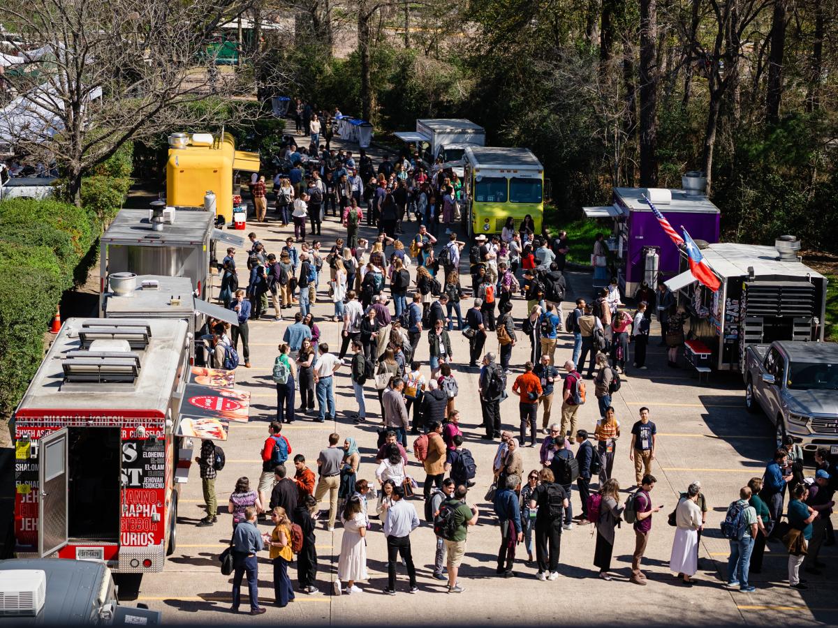 An overhead view of the Food Truck Village at LPSC. There are at least 10 food trucks along either side of a parking lot, each with long lines of customers from the convention. In the back, on the left, is another lot with white pop-up tents and tables for guests to eat their lunch.