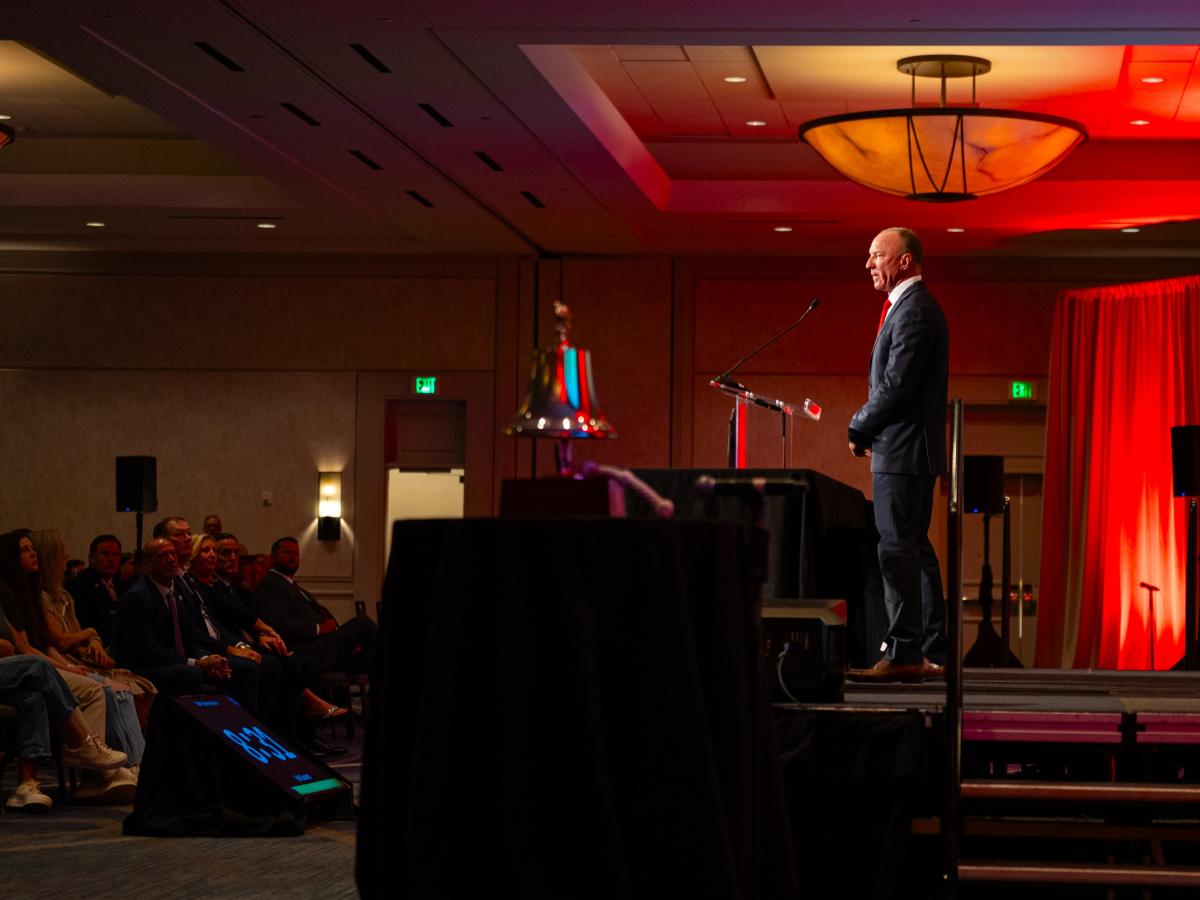 TWPFFA President Erik Secrest speaks at the Texas State Association of Fire Fighters 49th Biennial Convention. Secrest is in a black (or very dark navy) suit, standing behind a podium on a makeshift stage, addressing the TSAFF audience.