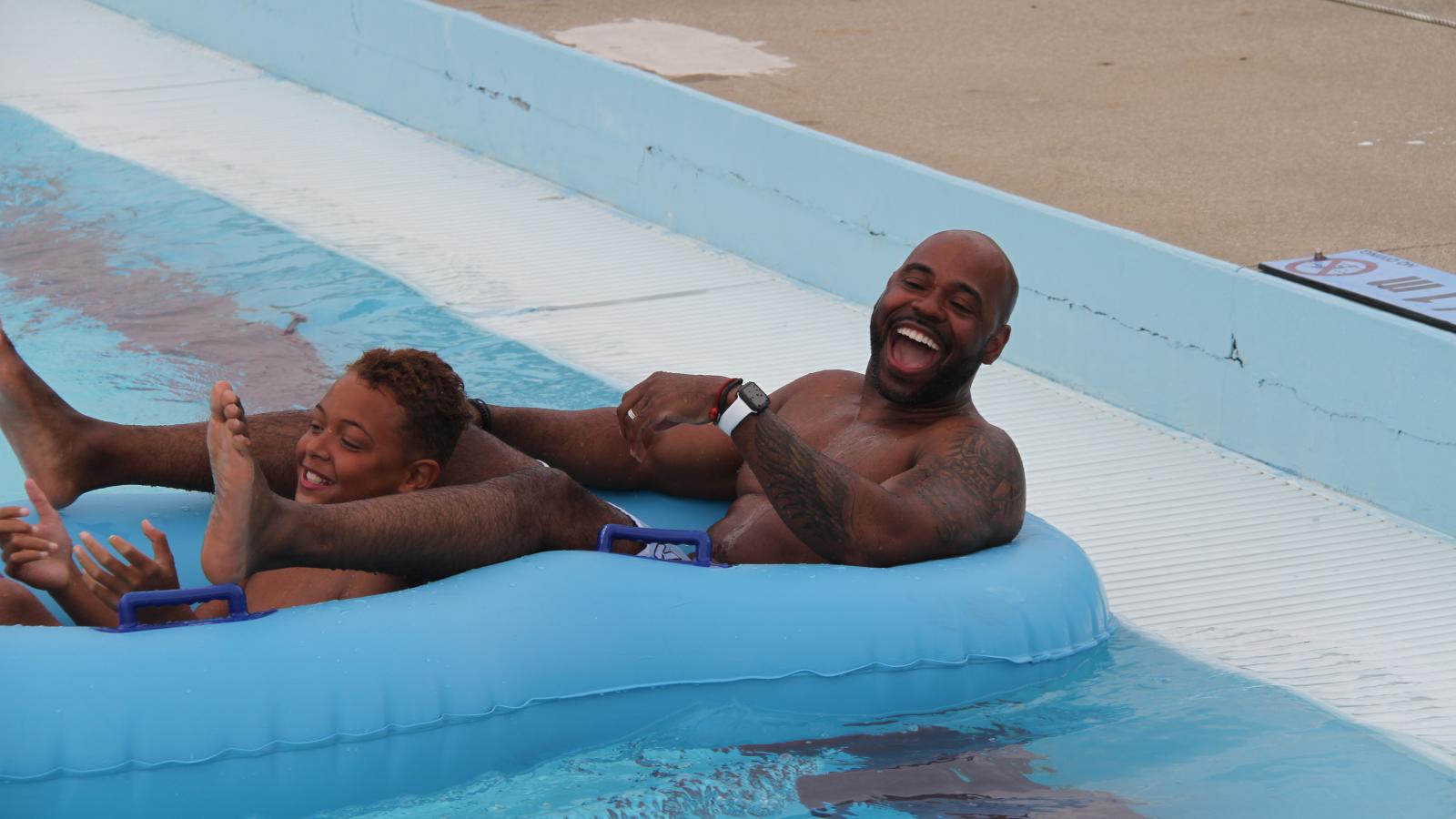 A dad and son in a two-seater inflatable, laughing, after having gone down a slide in Deep River Waterpark.