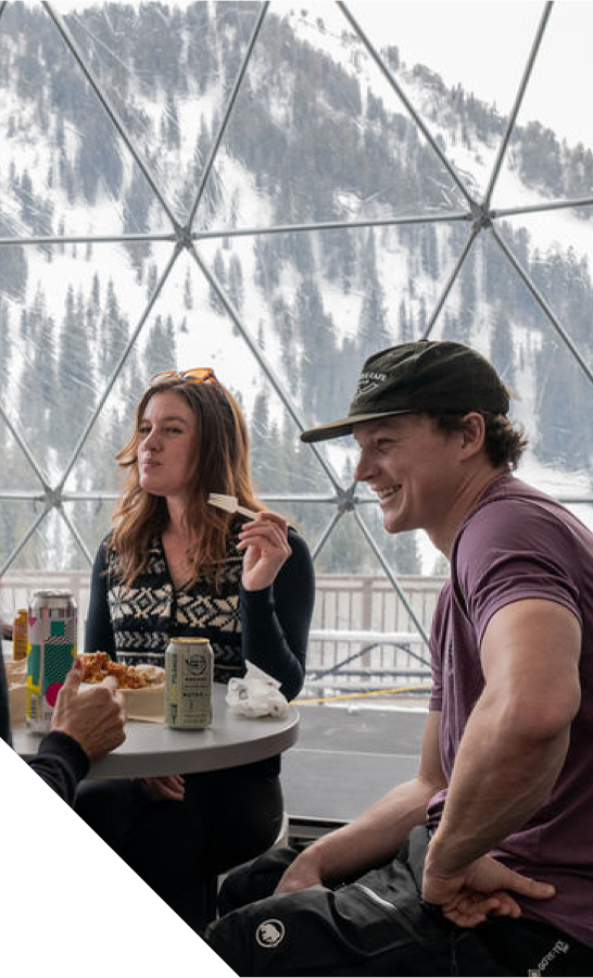 Two people sitting at a table with a snowy mountainside in the background