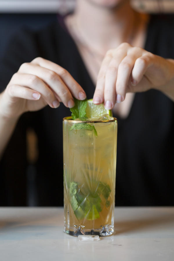 A bartender squeezes a lime into a golden cocktail in a tall glass with green garnish.
