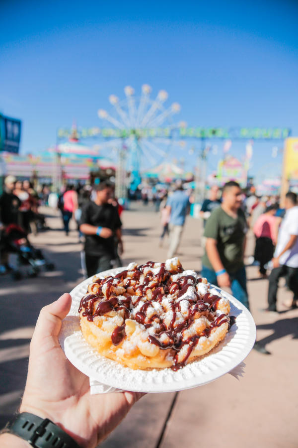 Person hold plate with funnel cake topped with chocolate and whipped cream
