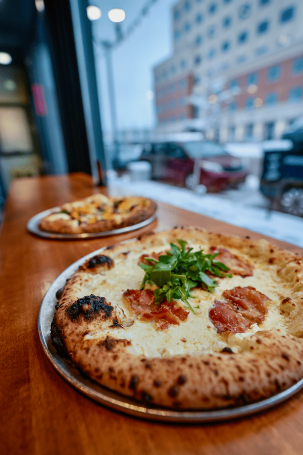 Two pizzas on a table by the window