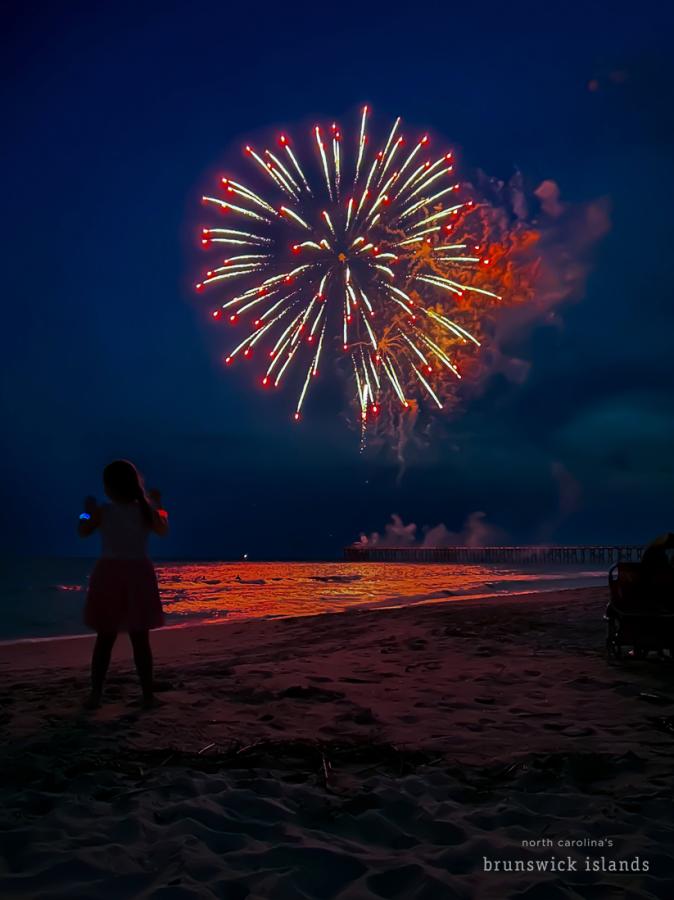 a young girl watching fireworks over the ocean from the beach on Oak Island, NC