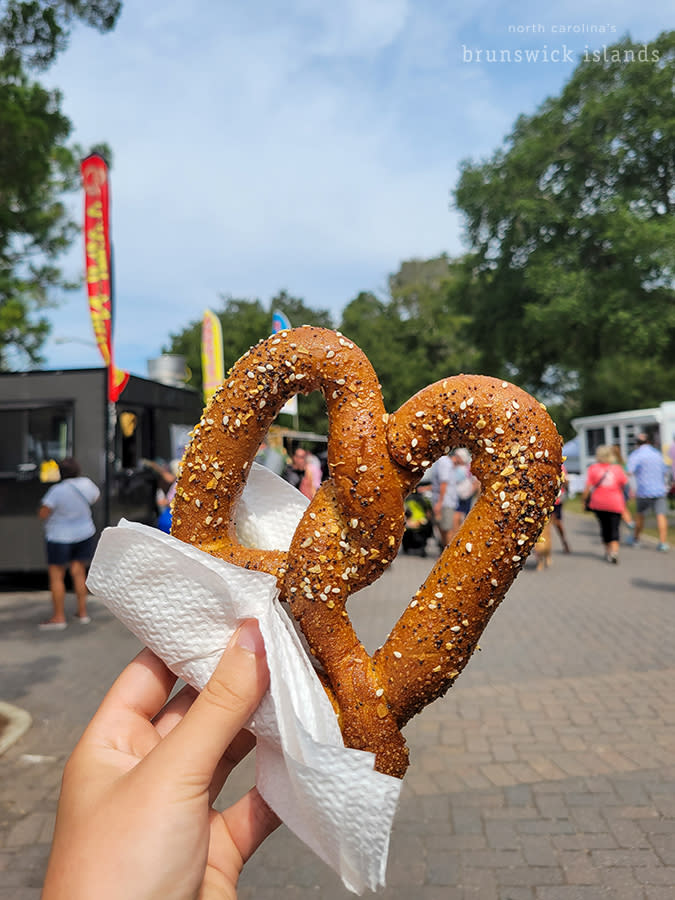 a hand holding a soft pretzel at an outdoor festival