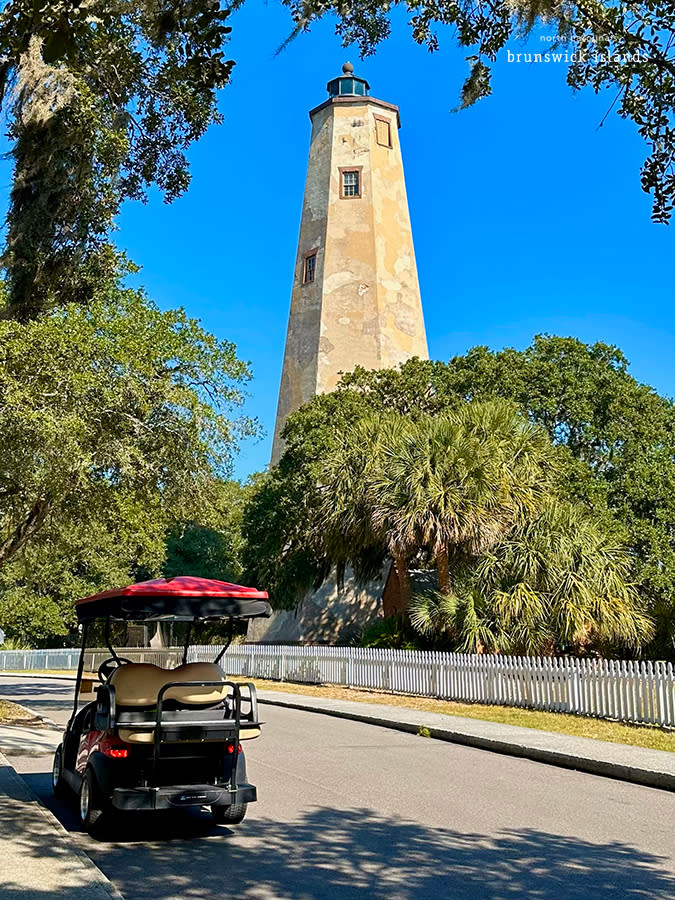 a red golf cart parked on the street in front of old baldy lighthouse on bald head island, nc
