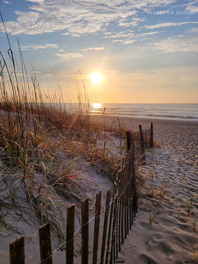 a wooden railing on the beach pointing towards a November sunrise over the ocean on Ocean Isle Beach, NC