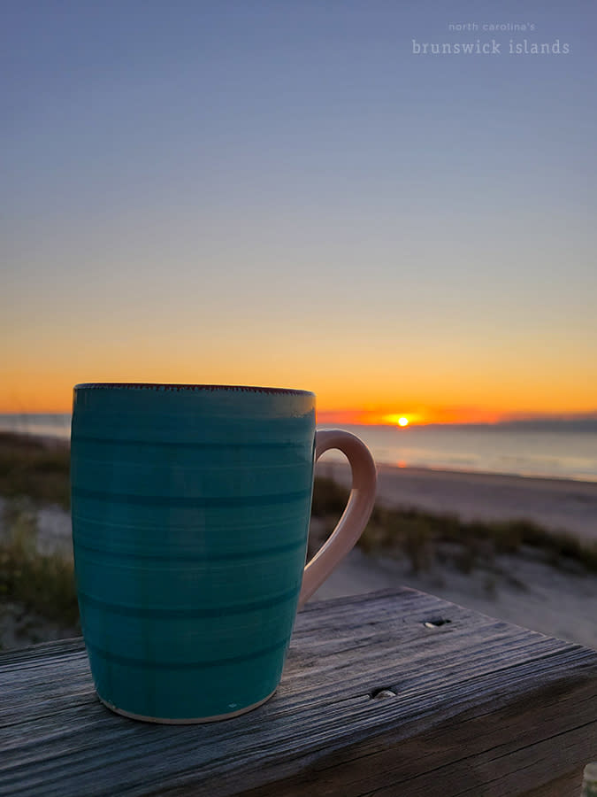 a cup of coffee on a wooden railing overlooking a sunrise over the ocean on Ocean Isle Beach