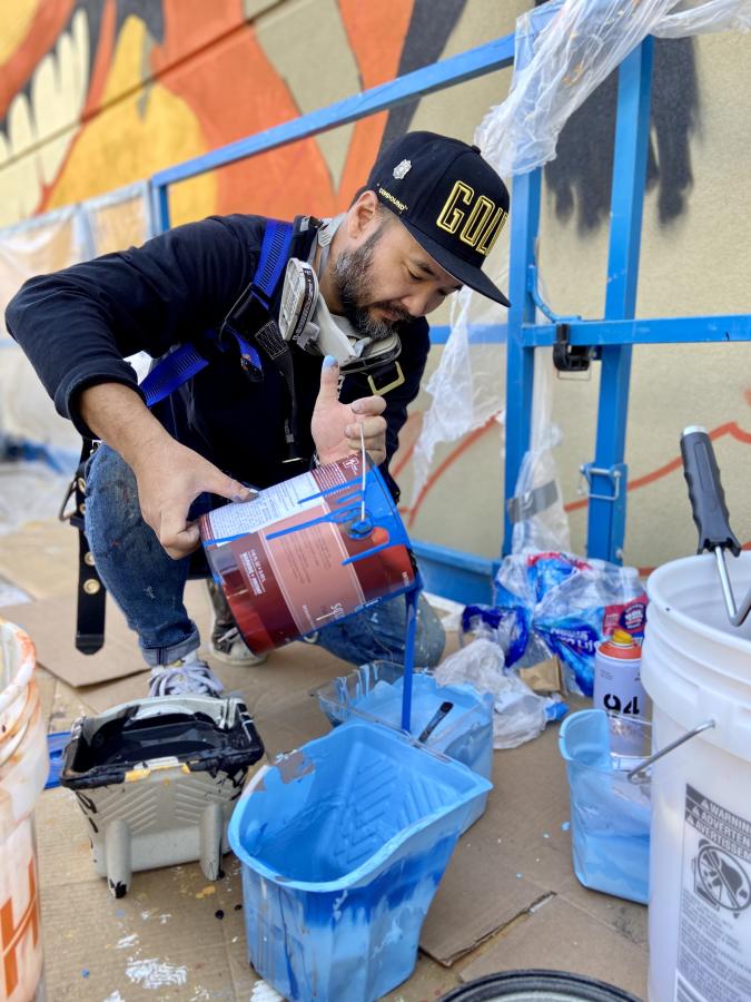 Artist pouring paint into tray in preparation of painting a large mural.