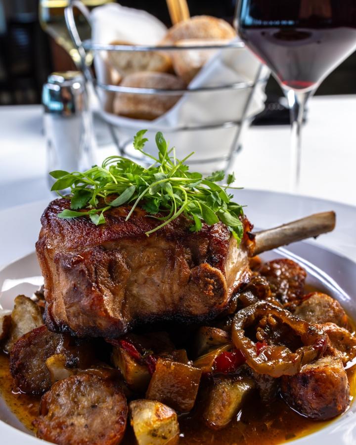 a bone in pork chop topped with greens sitting on a bed of roasted potatoes and veggies from LeVolte Oceanfront Dining on Ocean Isle Beach, NC