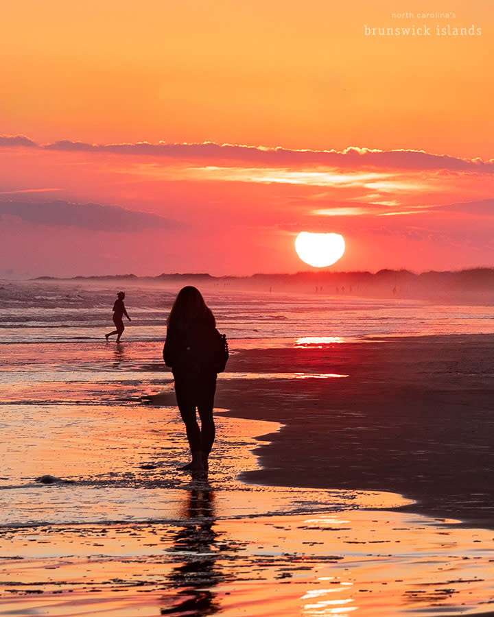 a person walking towards a large setting sun on the horizon on Sunset Beach, NC