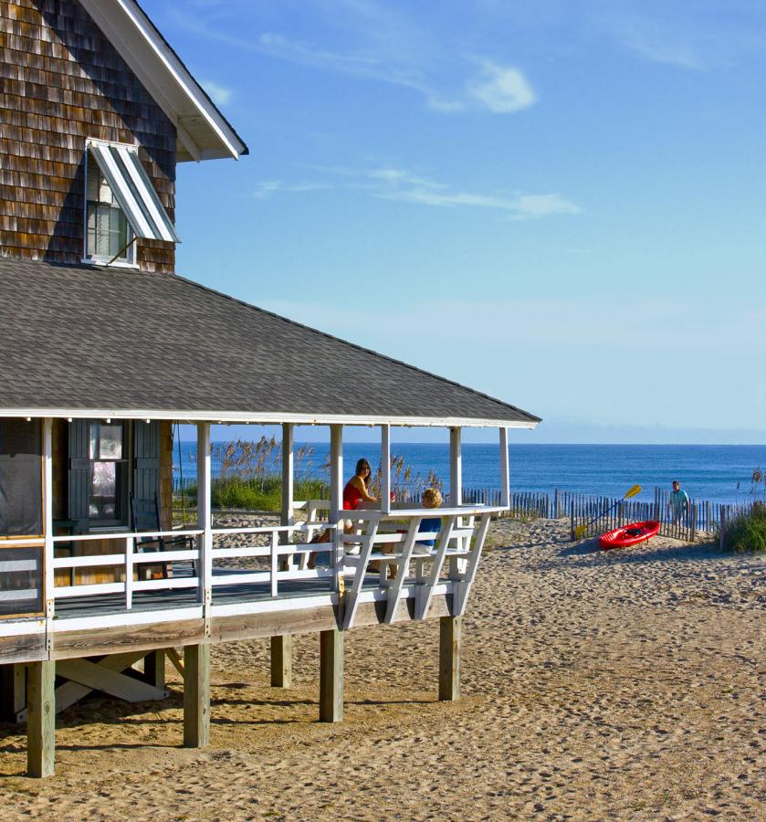 Visitors enjoy the fresh air and view from the wrap-around porch of their Outer Banks vacation rental.