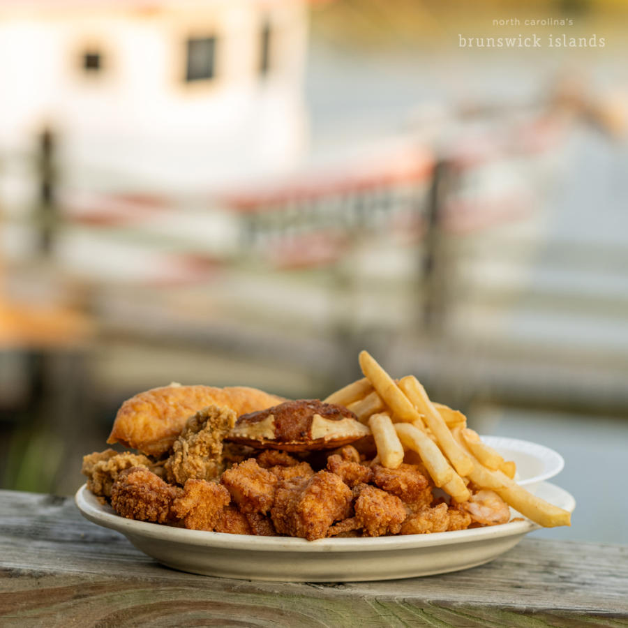 a plate of fried seafood and fries in front of a shrimp boat