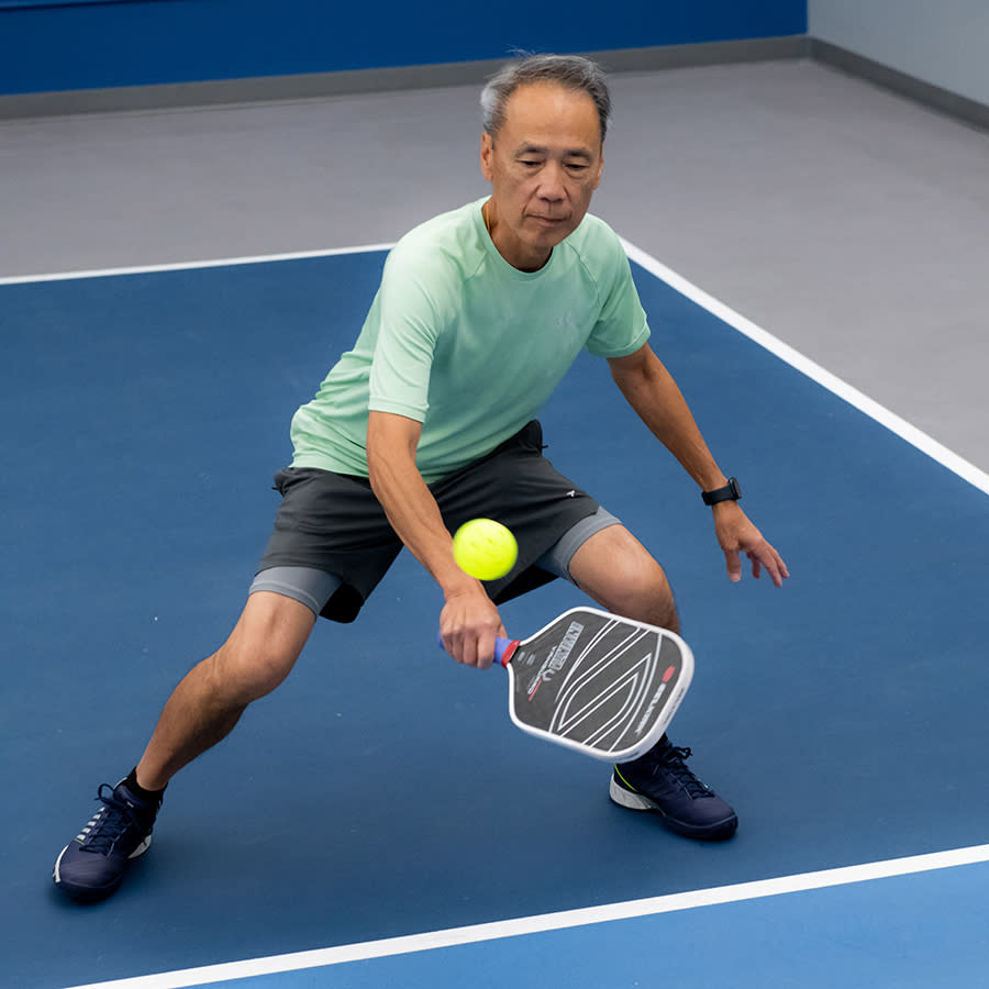 a man crouching to return a ball in pickleball