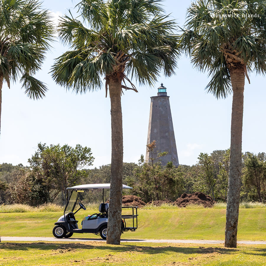 a gold cart parked on a road between palm trees with a triangular stone lighthouse in the background