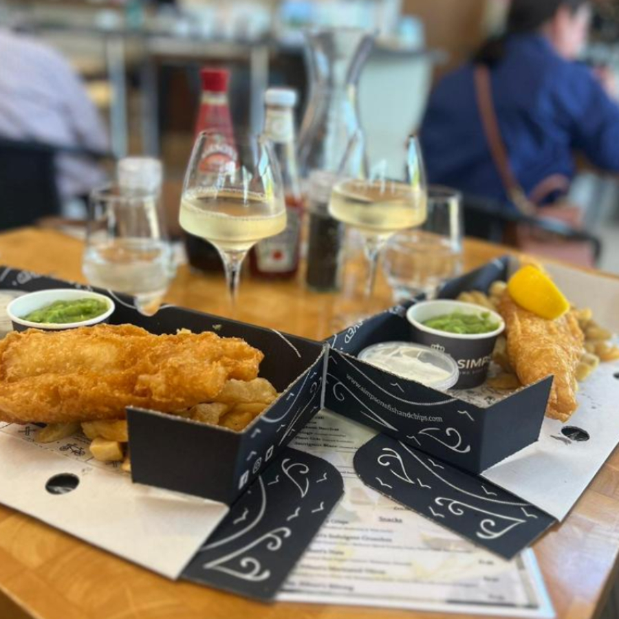 Two boxes of delicious fish and chips on a table with glasses of chilled white wine from Woodchester Valley Vineyard