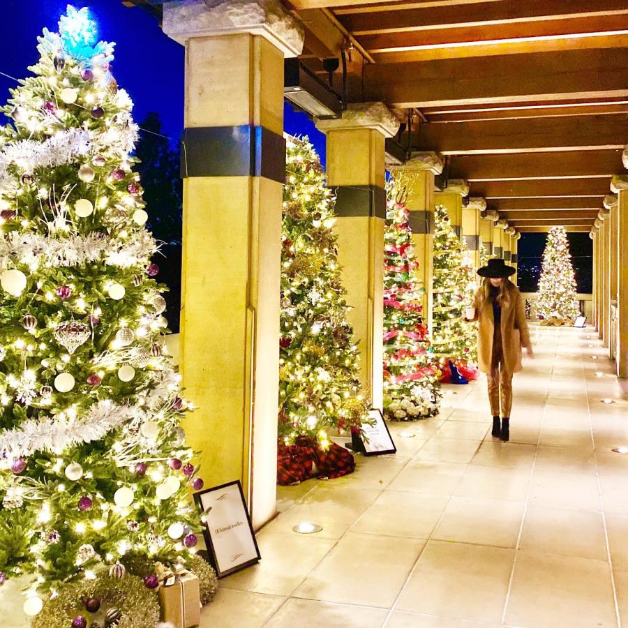 A woman walks along a patio lined with decorated Christmas trees at Mission Hill Holiday Event