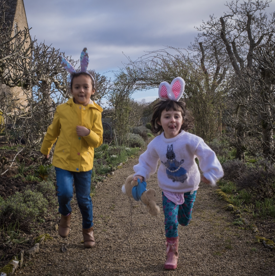 Two children wearing bunny ears run through the kitchen garden at Cogges Manor Farm