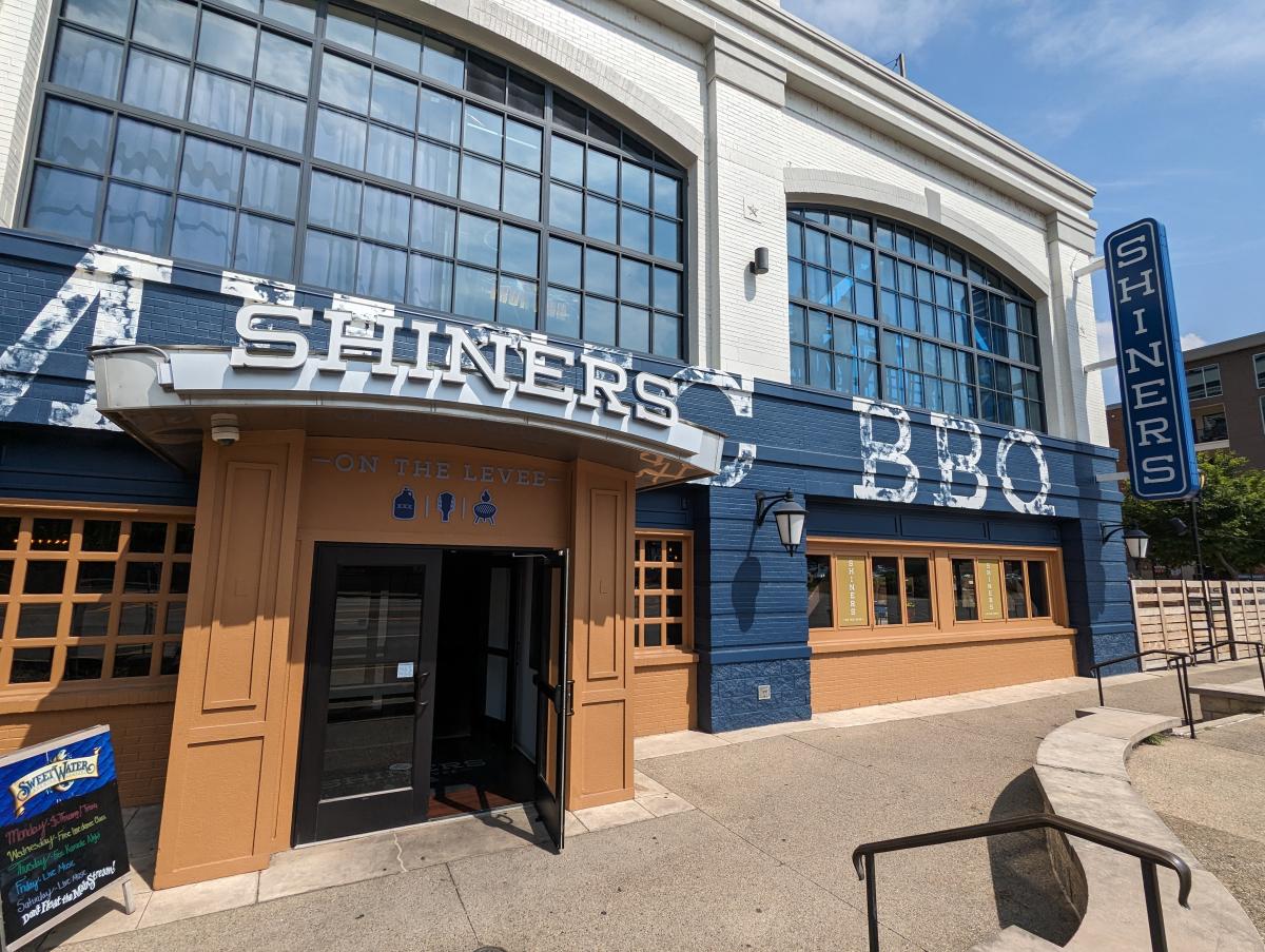 Image is of the outside of Shiners on the Levee with the front and hanging sign that says "Shiners" on the side.