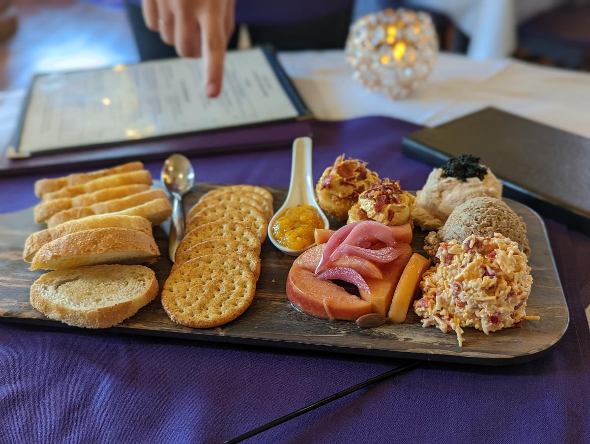 Charcuterie board of pimento cheese, crackers, bread, deviled eggs, salmon mousse on a purple tablecloth