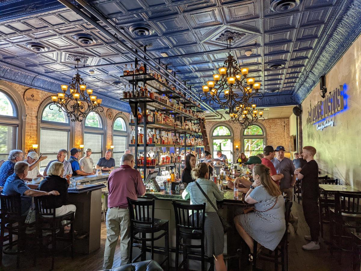 The bourbon bar at Smoke Justis with six shelves of bourbon in the center, surrounded by a wooden bar seated with many customers