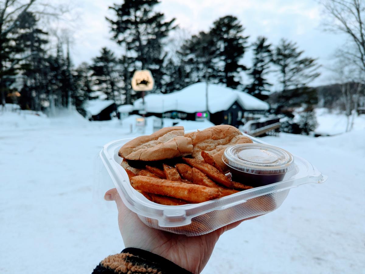 a hand holds up a to go box containing a sandwich and fries