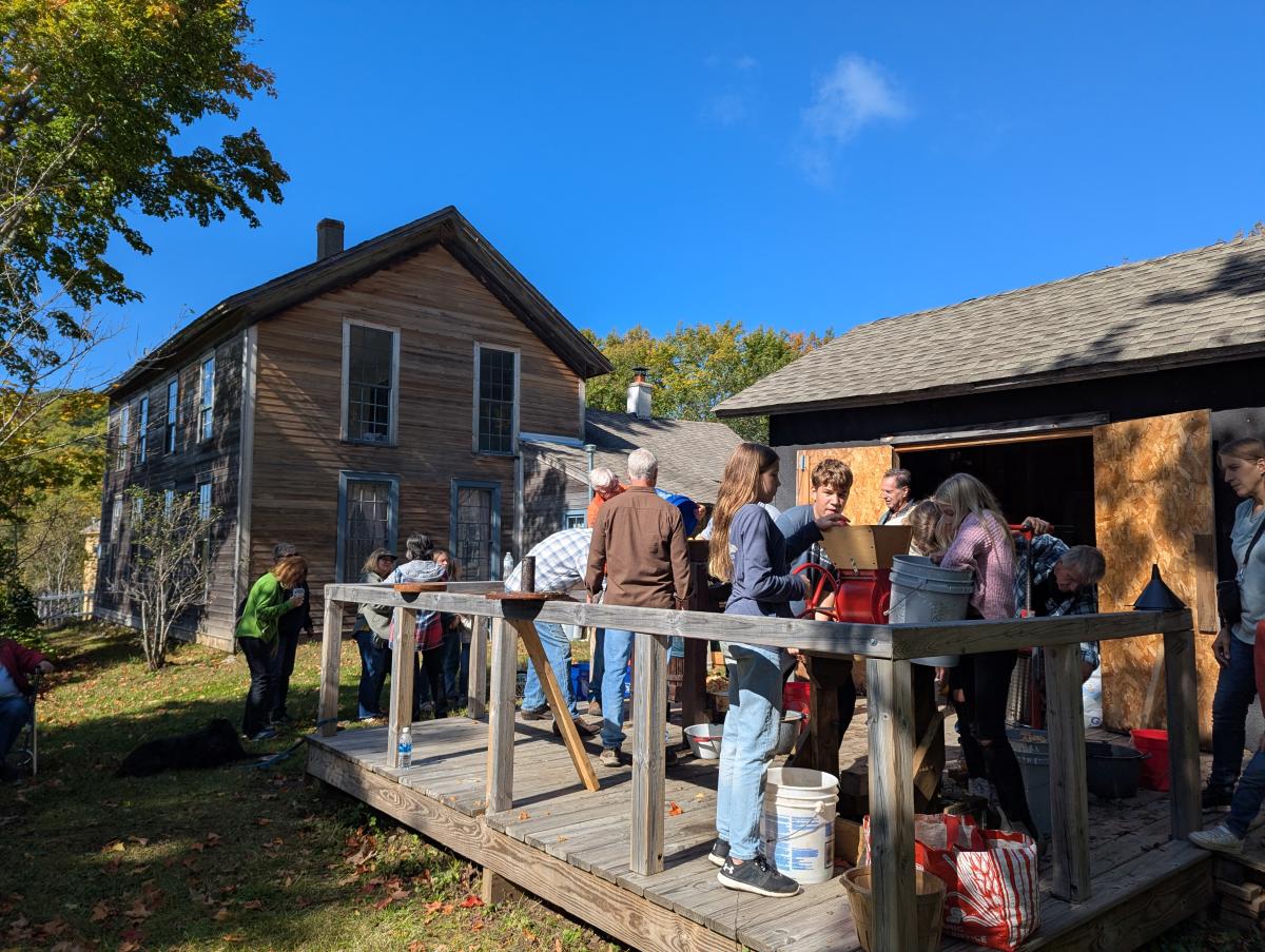 people fill the back yard of a historic mining house to press apple cider