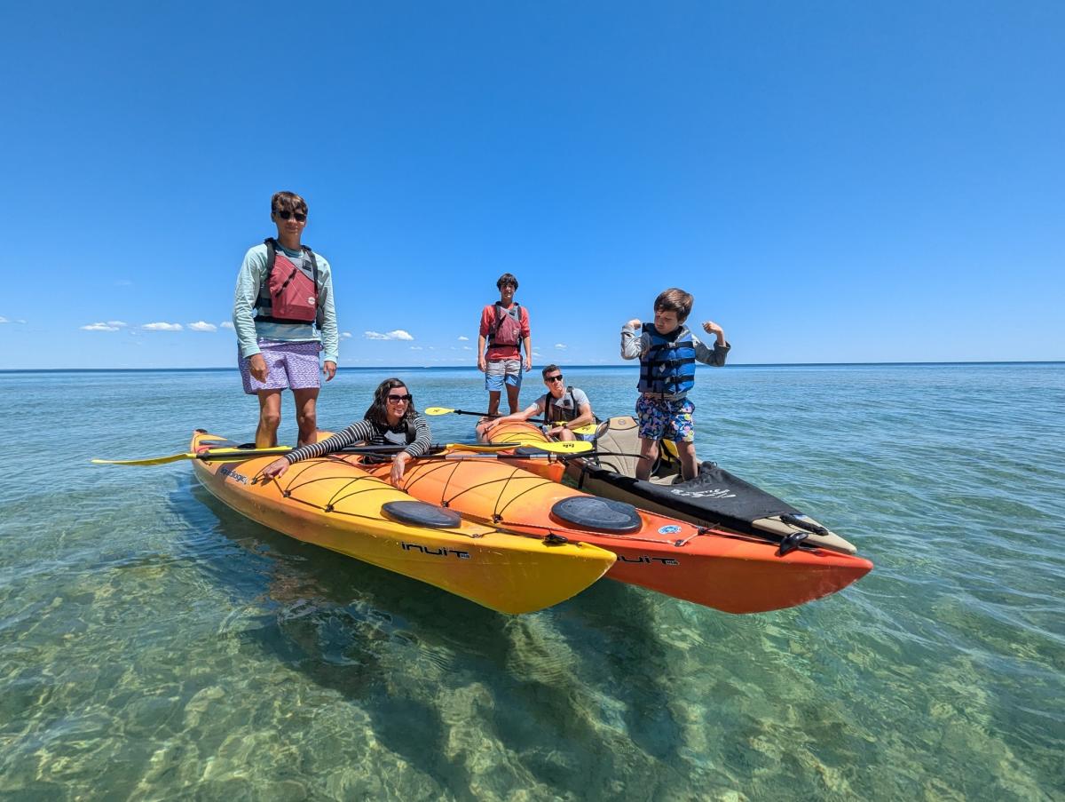 Kids stand up in a flotilla of three kayaks on the water off Mackinac Island