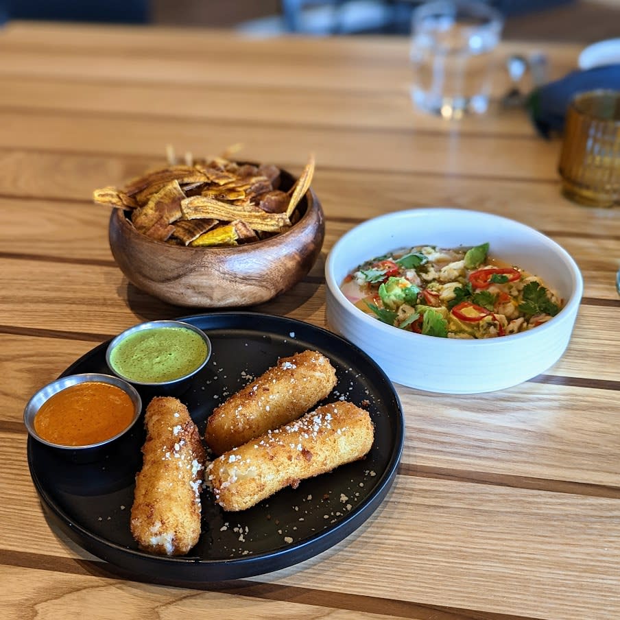 Image is of the queso croquetas on a plate with two dipping sauce and ceviche with platina chips.