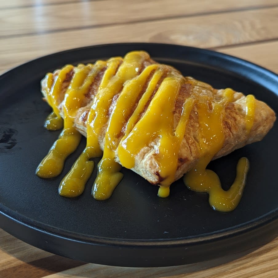 Image is of the Mango Pastelito which is a flakey pastry with cinnamon and mango drizzle.