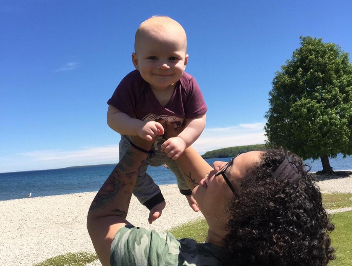 A baby smiles while being held by a woman on the beach at Mackinac Island’s Windermere Point
