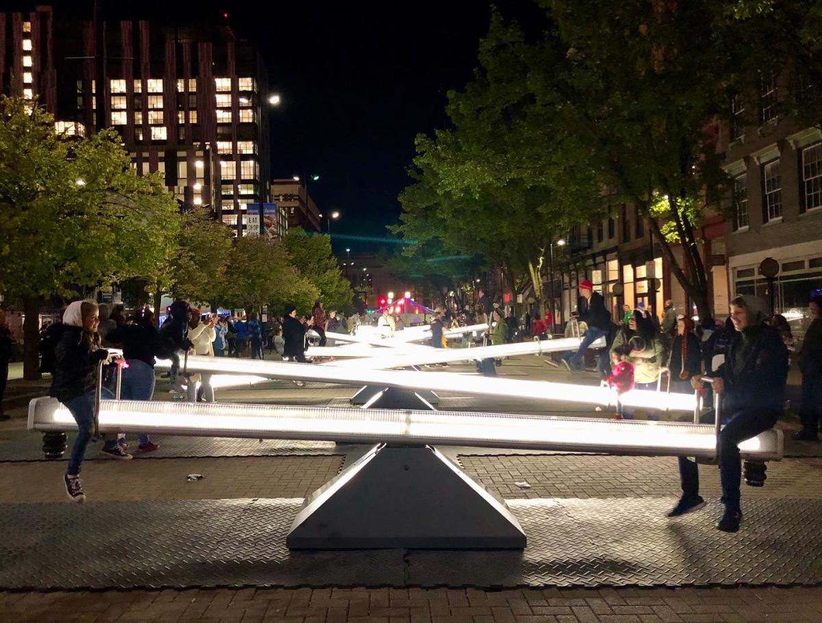 Night time shot of a row of illuminated teeter-totters with people using them at BLINK Cincinnati