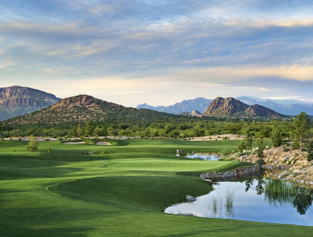 landscape photo of landscaped golf course scattered with blue ponds. Desert Mountains surround the gold course on the horizon