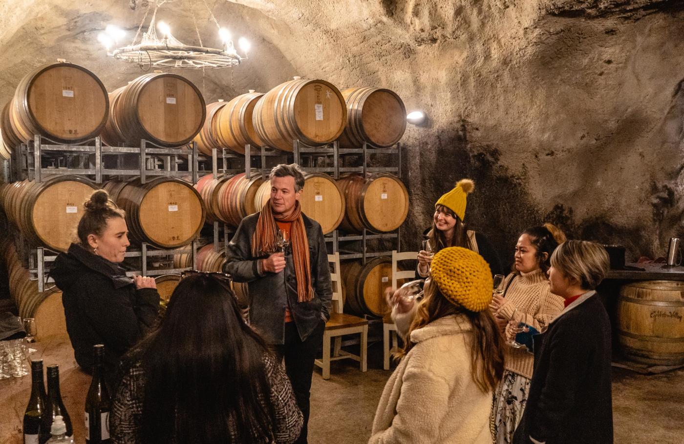Group of people on a wine tour in an underground wine cave with wine barrels around