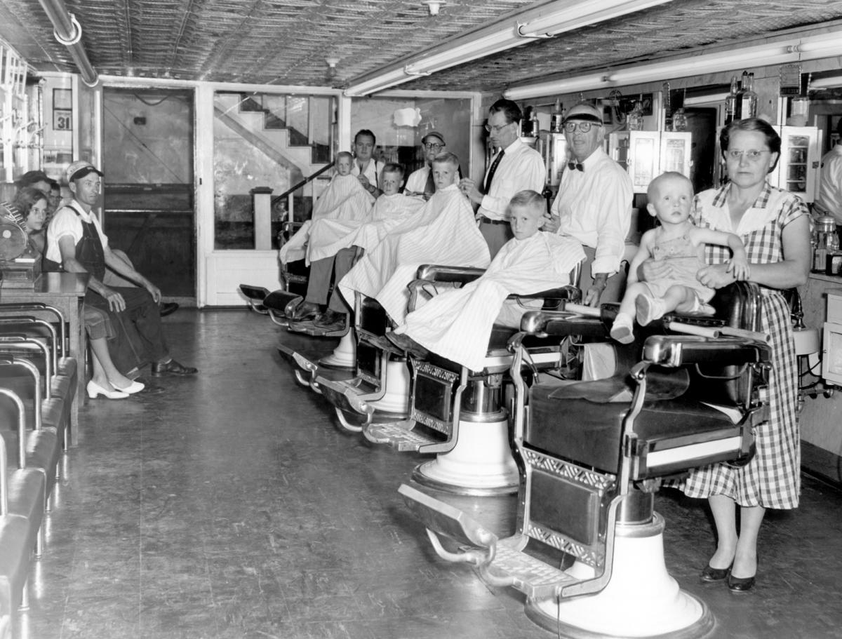 Five Clayton boys in barber capes getting haircuts from four barbers at Hedden’s Barber Shop in Sylva, NC, in the mid-1950s, with their parents nearby