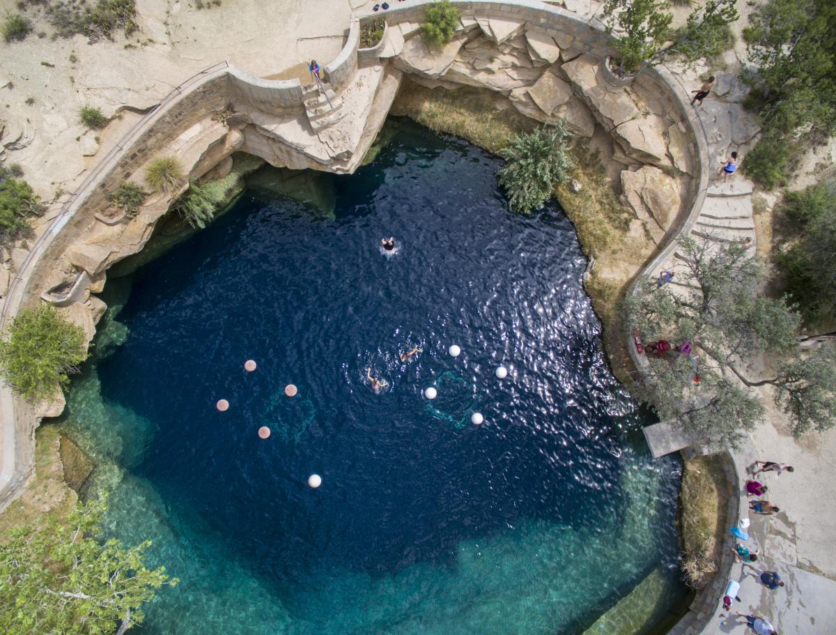 A aerial view of a vibrant blue pool of water with people swimming in it.