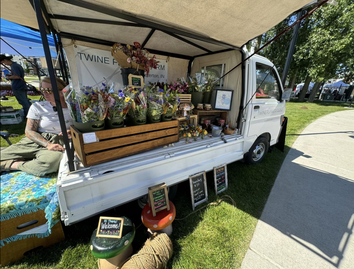 A woman sits on a flower truck with an open side. Bunches of flowers are displayed.