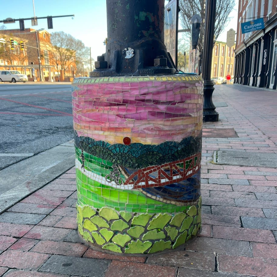 The "Ginkgo Greenway" mosaic adorns a light pole base in downtown Athens, using green and pink glass pieces to depict Athens' walking and biking paths.