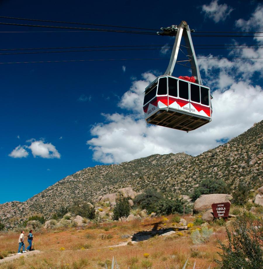 A couple hiking looks up at the Sandia Peak Aerial Tramway overhead