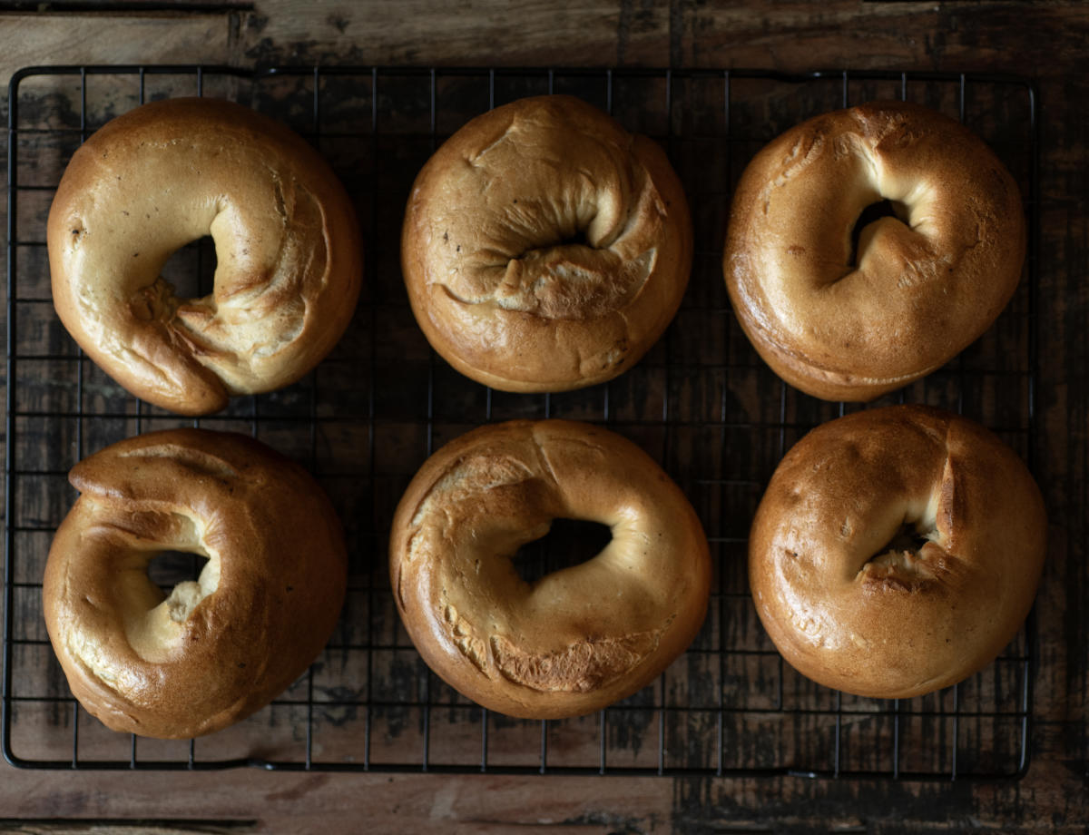 Six freshly baked bagels rest on a black wire cooling rack.