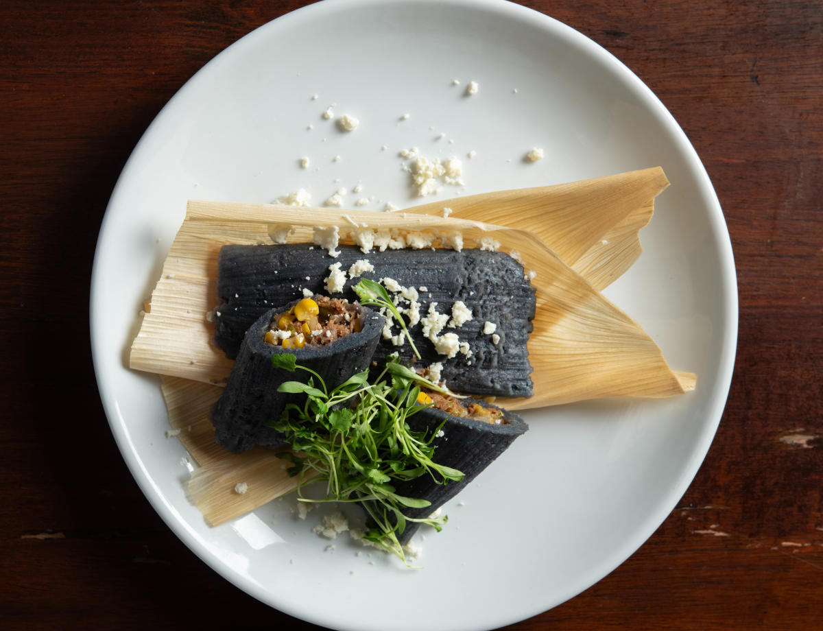 Blue corn rabbit tamales wrapped in husks and topped with colorful garnishes.