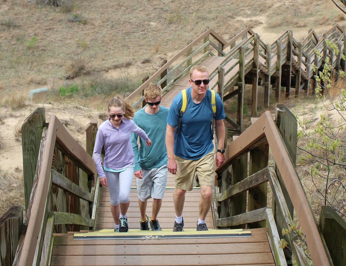A man and two young teens walk up stairs on a trail