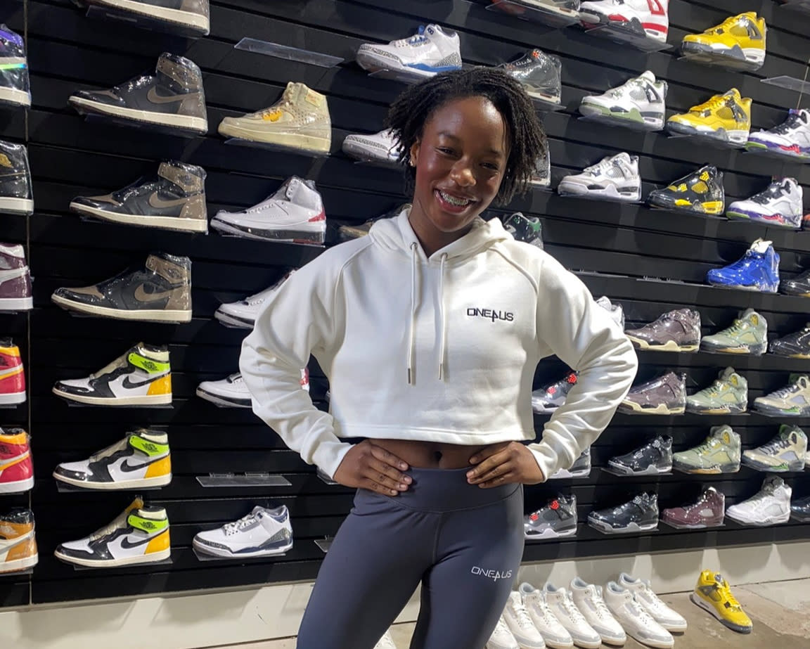 A girl poses in front of a wall of shoes on display for sale at Knockout Sneaker Boutique