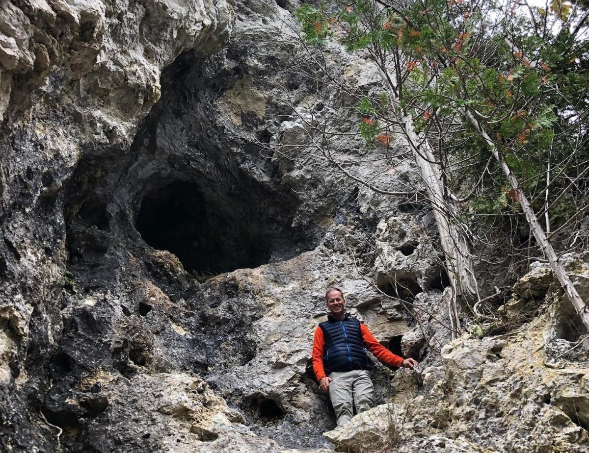 A man stands beneath the opening to a rocky cave in Mackinac Island State Park