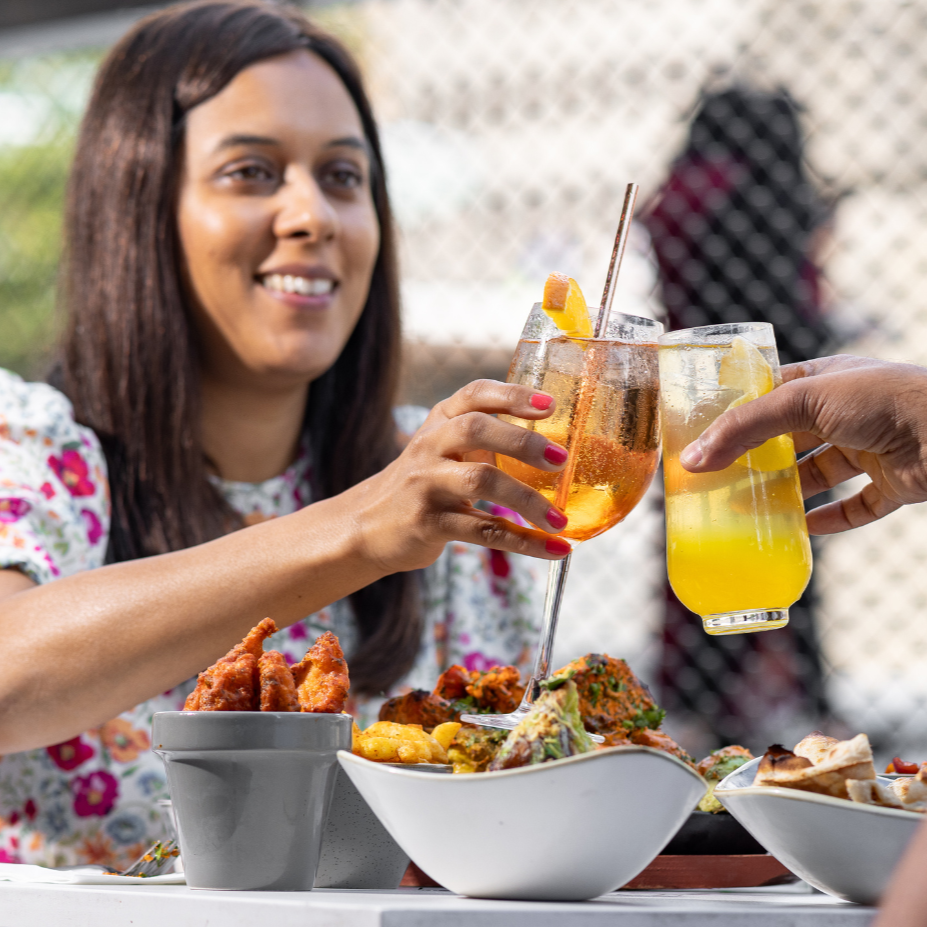 Two people toasting drinks outside Tap and Tandoor
