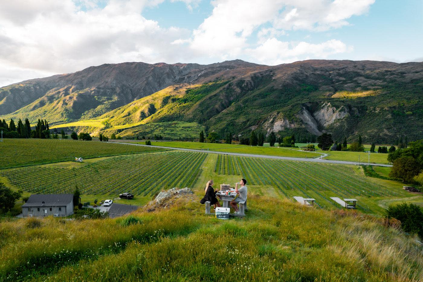 Couple dining at a picnic table overlooking Kinross Winery in the Gibbston Valley