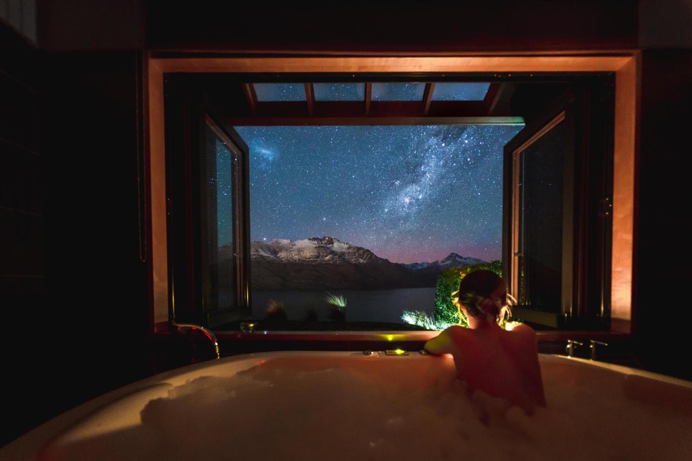 Person in a bath at night with starry view of lake and mountains