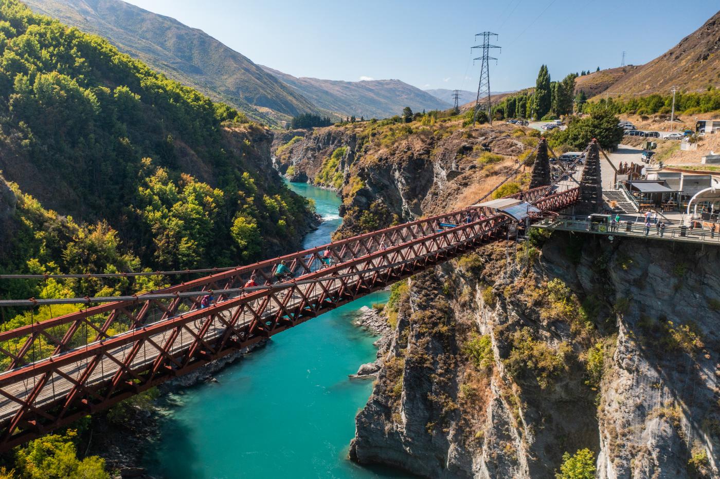 People biking over a bridge with vibrant blue water below